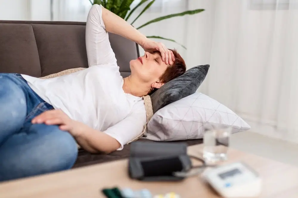 Senior woman in bed, holding head, experiencing distress due to brain abnormalities.